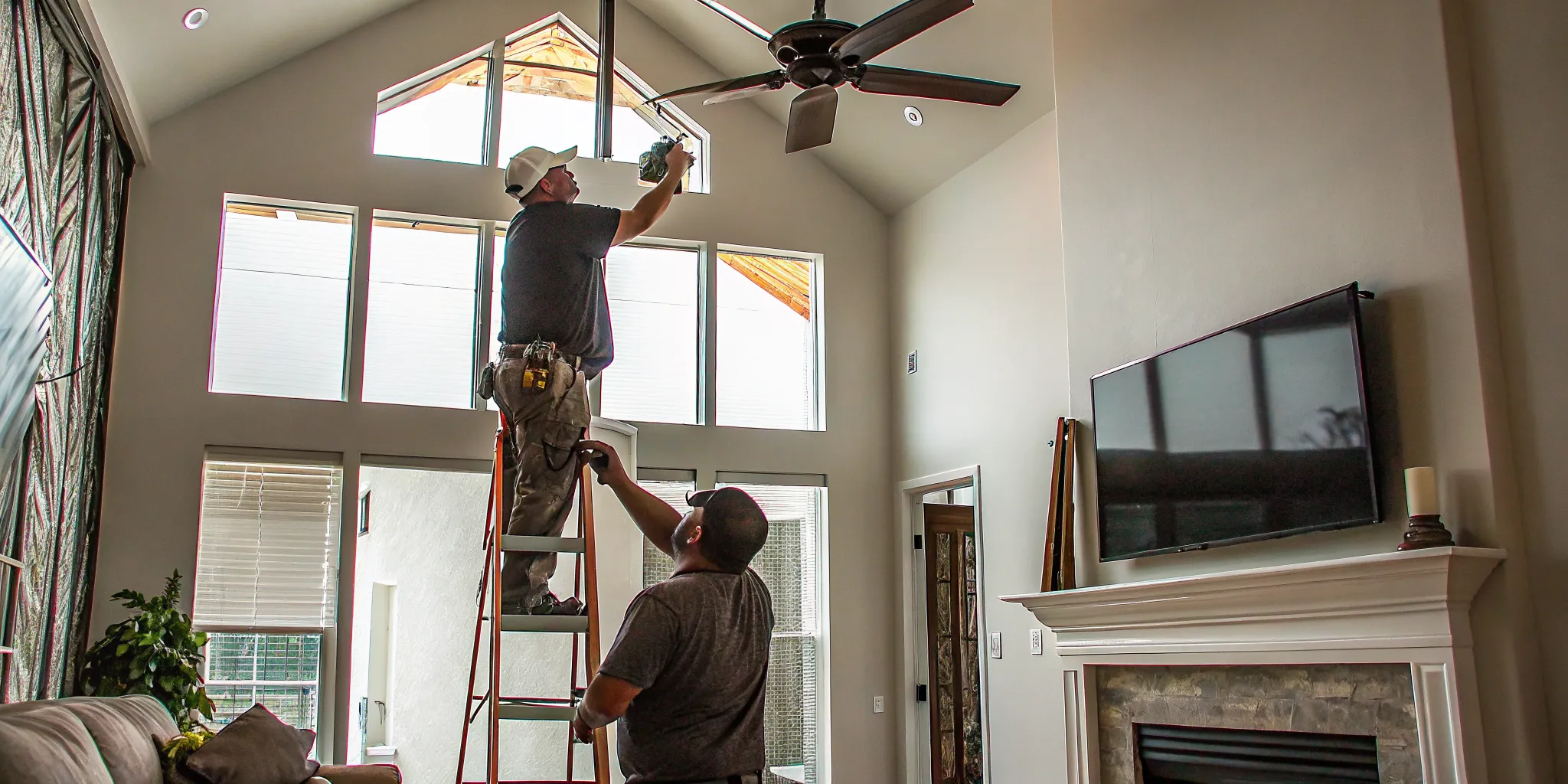 Electrician installing a ceiling fan on a tall vaulted ceiling