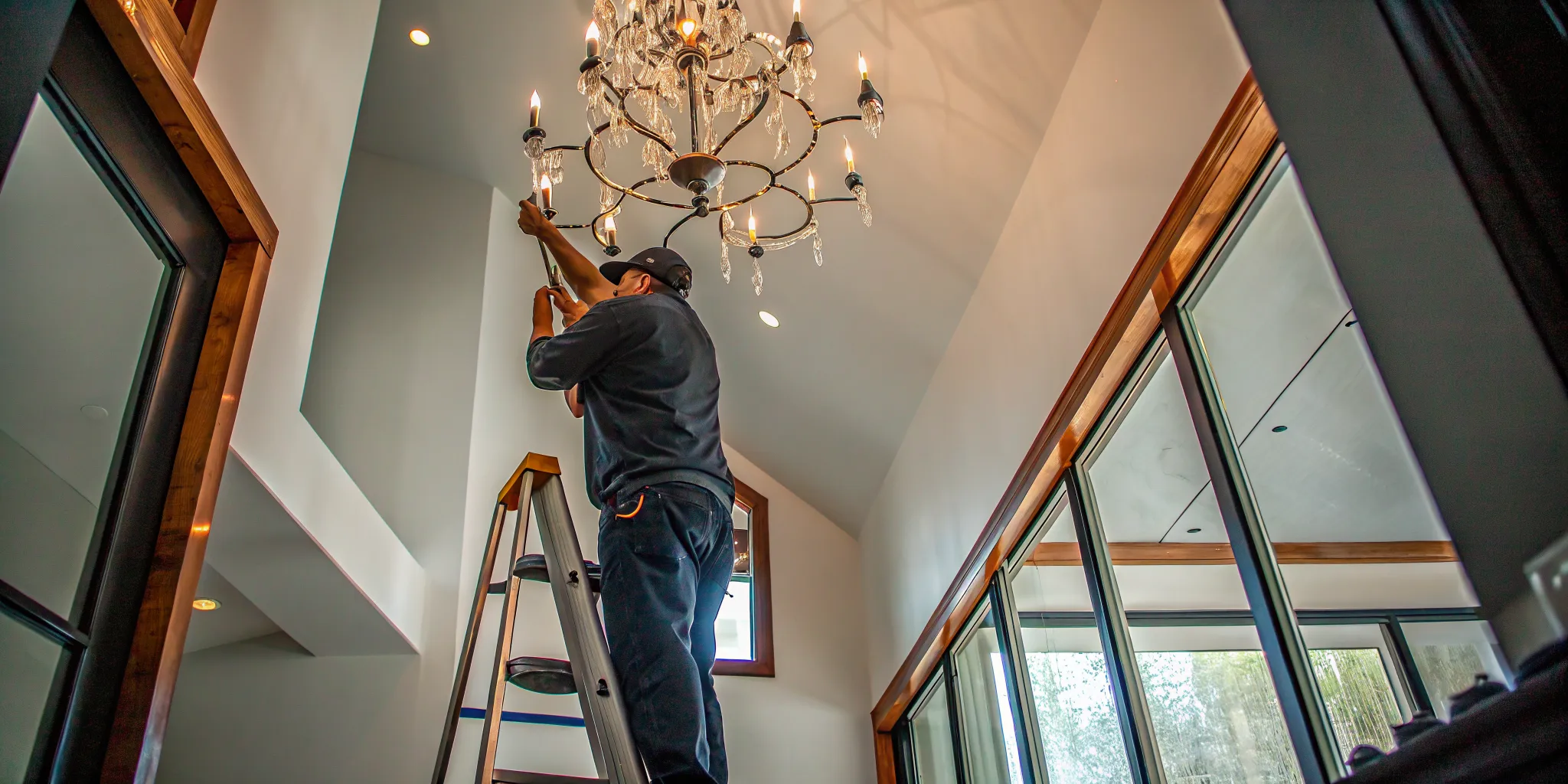 Electrician installing a chandelier in a high-ceiling DFW home